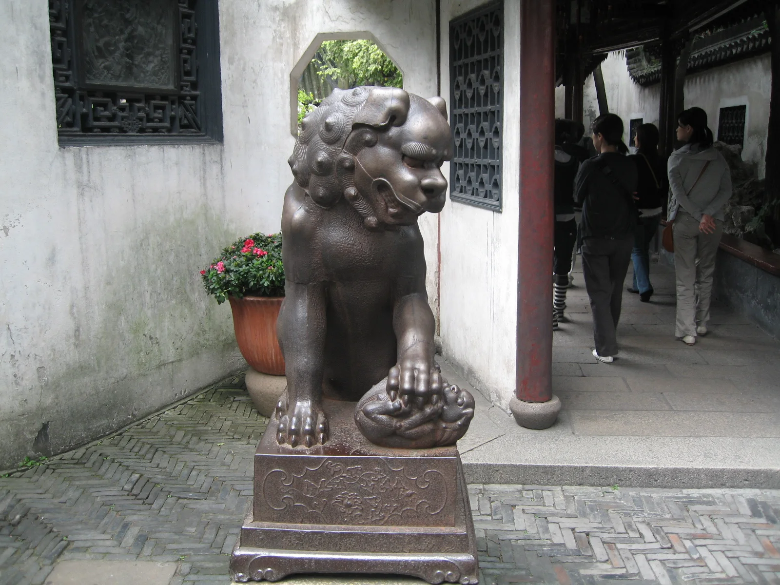 A dark lion-like guardian sculpture stands on a pedestal beside a doorway in a white garden wall.