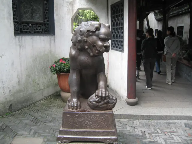 A dark lion-like guardian sculpture stands on a pedestal beside a doorway in a white garden wall.
