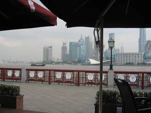 Dark terrace umbrellas frame a red riverside railing and a hazy skyline across the water.