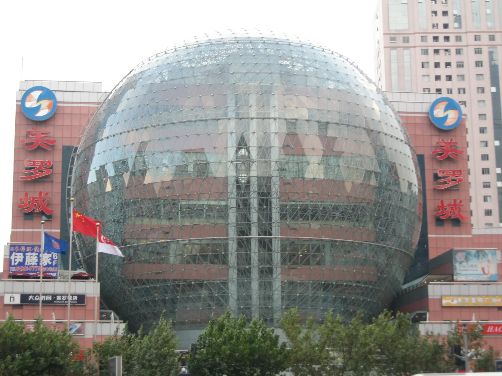 A large spherical glass facade forms part of a shopping building with red panels and surrounding towers.