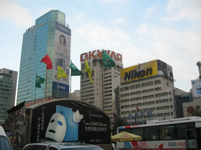 High-rise facades carry large advertisements above traffic, including a bus and a prominent yellow Nikon sign.