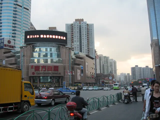 Buses, cars and scooters crowd a street lined with tall buildings and advertising signs.