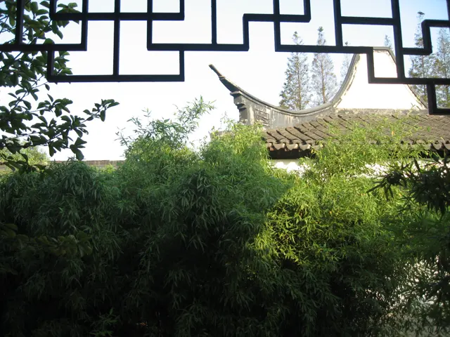Geometric wooden latticework frames greenery and a curved tiled pavilion roof beyond.