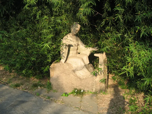 A pale carved stone figure rests among rocks and dense bamboo beside a garden path.