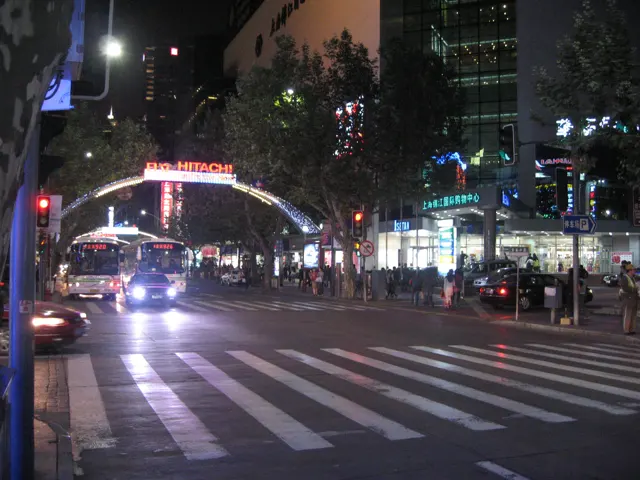 A zebra crossing spans a busy night-time road beneath an illuminated arch and bright street lamps.