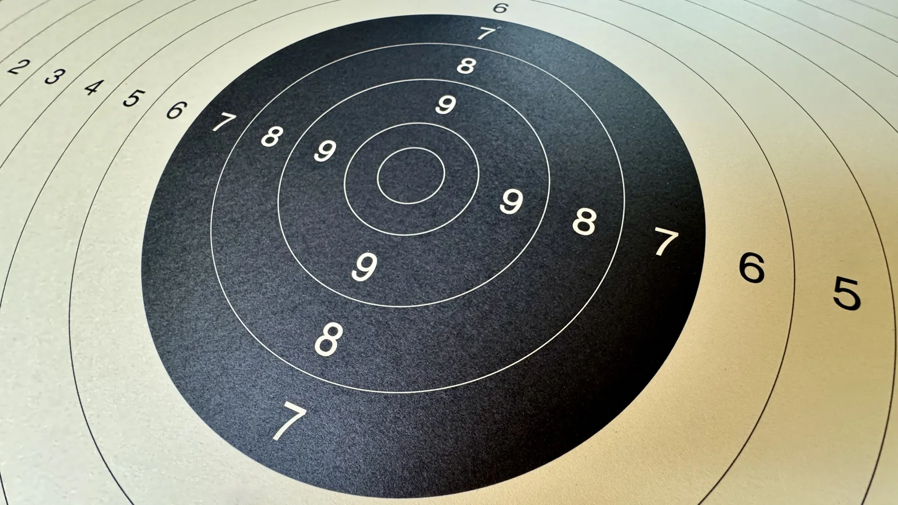 An oblique close-up of a paper target, with a black centre, fine concentric rings and white scoring numbers.