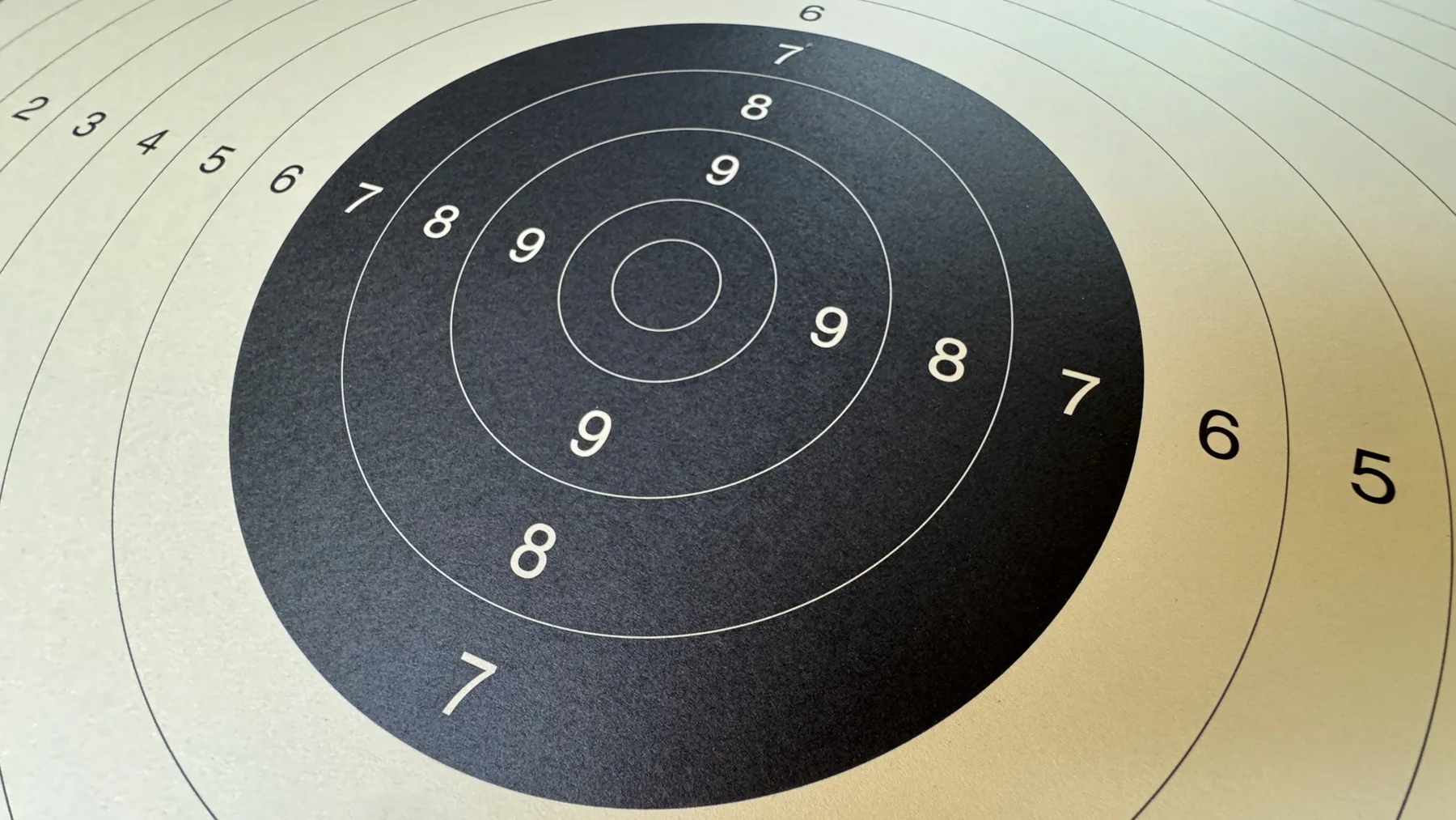 A black circular target on cream paper, photographed at an angle with numbered rings extending across the frame.