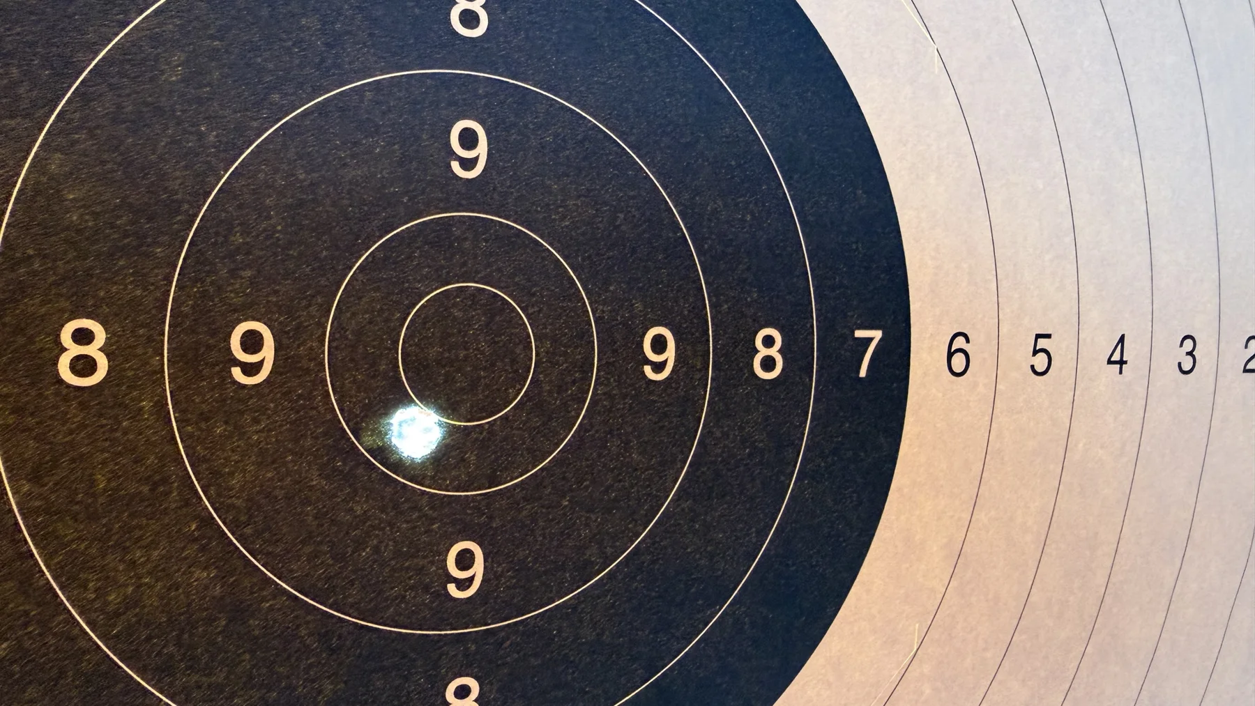A close-up of a bright hole near the centre of a black target, surrounded by fine white circles and scoring numbers.