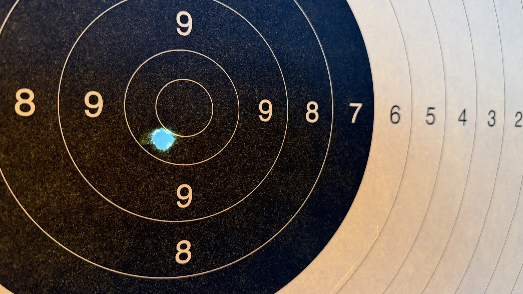 A small blue-white opening interrupts the dark paper just below and left of the central circle, with scoring numbers extending to the right.