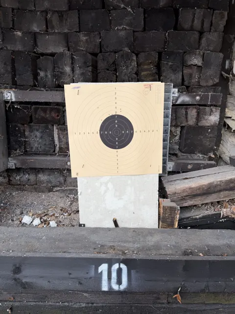A portrait view of a paper target on a pale stand against a timber backstop, with the number 10 painted on the lower beam.