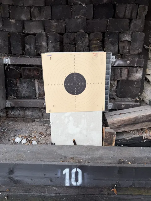 A second portrait view of the target and its pale support, framed by stacked timber and a lower beam marked 10.