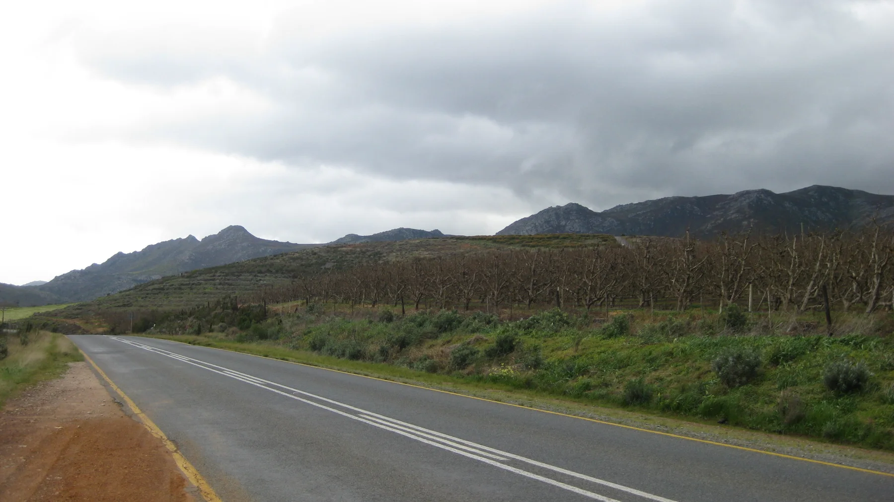 A quiet road follows cultivated fields toward distant hills beneath an overcast sky.