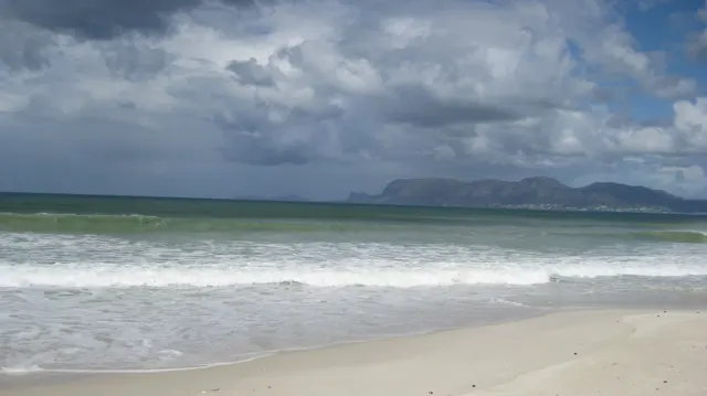 White surf follows a gently curving sandy beach with mountains on the far horizon.