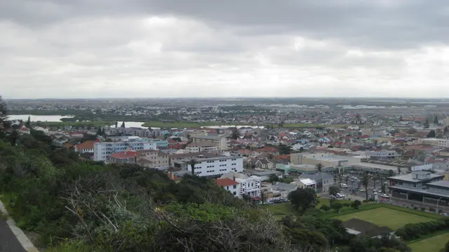 Dense town buildings spread beyond a green foreground slope under gray skies.