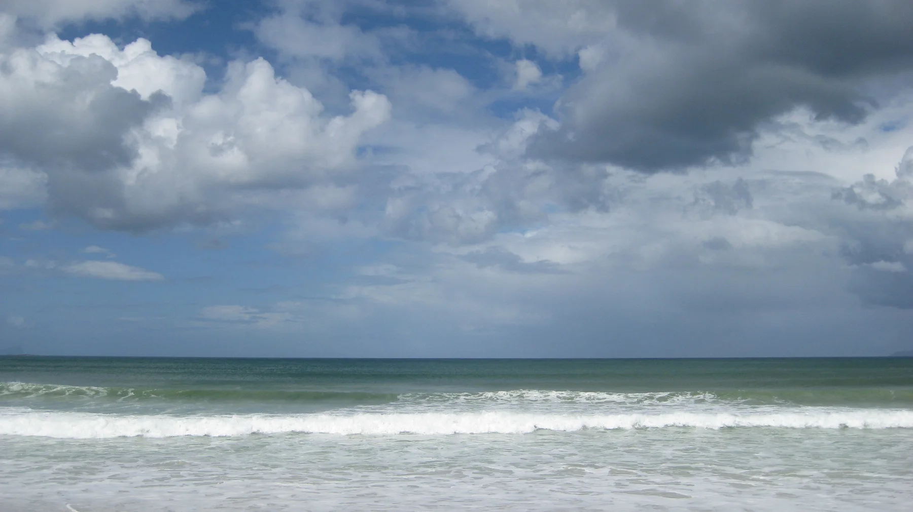 White surf rolls beneath a broad sky of layered clouds.
