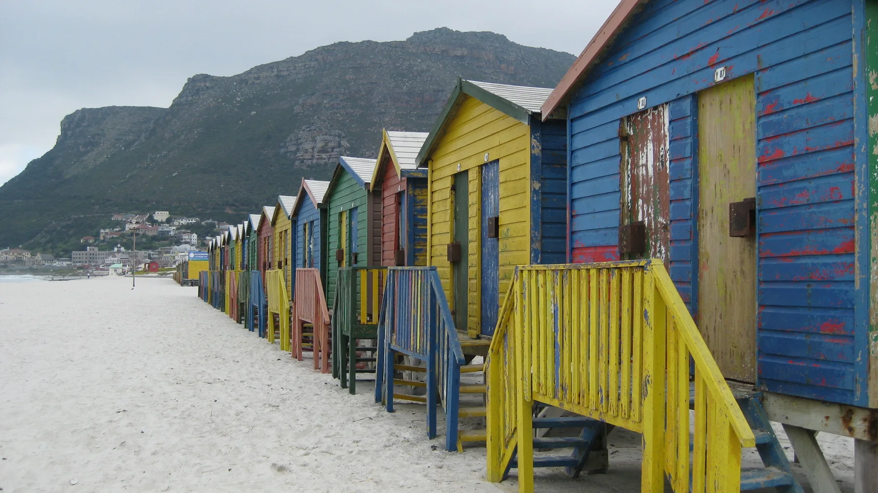Yellow steps lead to colorful wooden beach huts beside the sand.