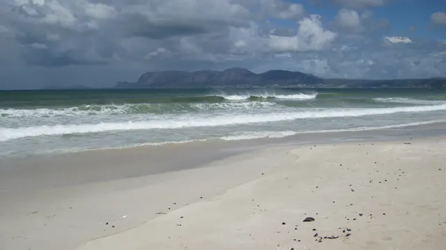 A broad sandy shore meets white waves beneath dark clouds.