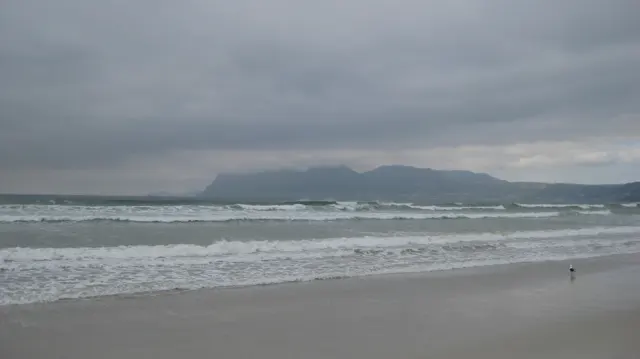 A distant mountain silhouette stretches behind gray water and white surf.