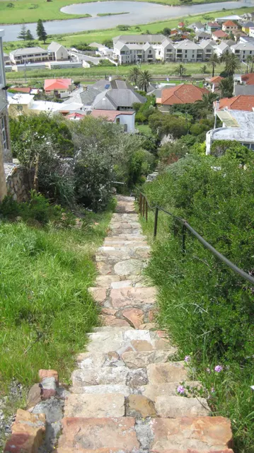 A narrow stone stairway descends between green banks toward town roofs.