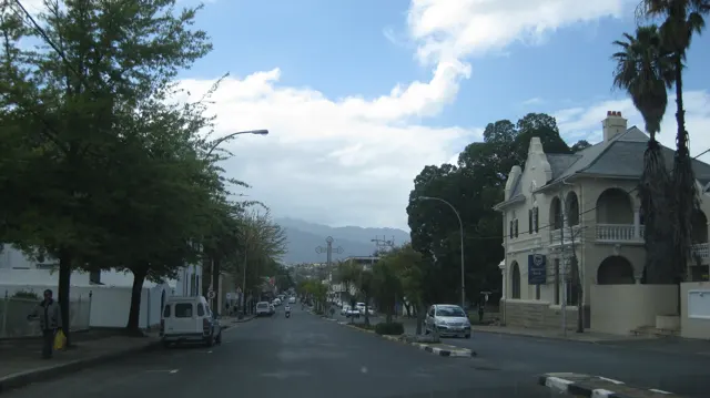 An ornate pale corner building faces a leafy street with hills beyond.