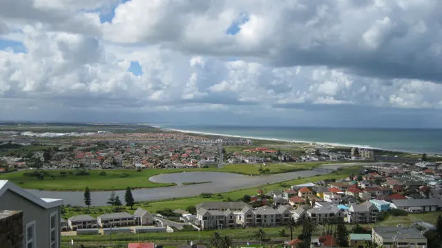 A town and green playing fields spread toward the coast beneath billowing clouds.