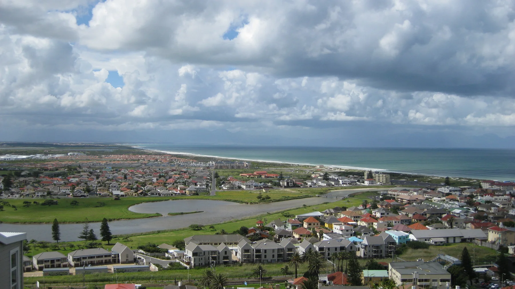 Green playing fields interrupt dense town roofs near the ocean.