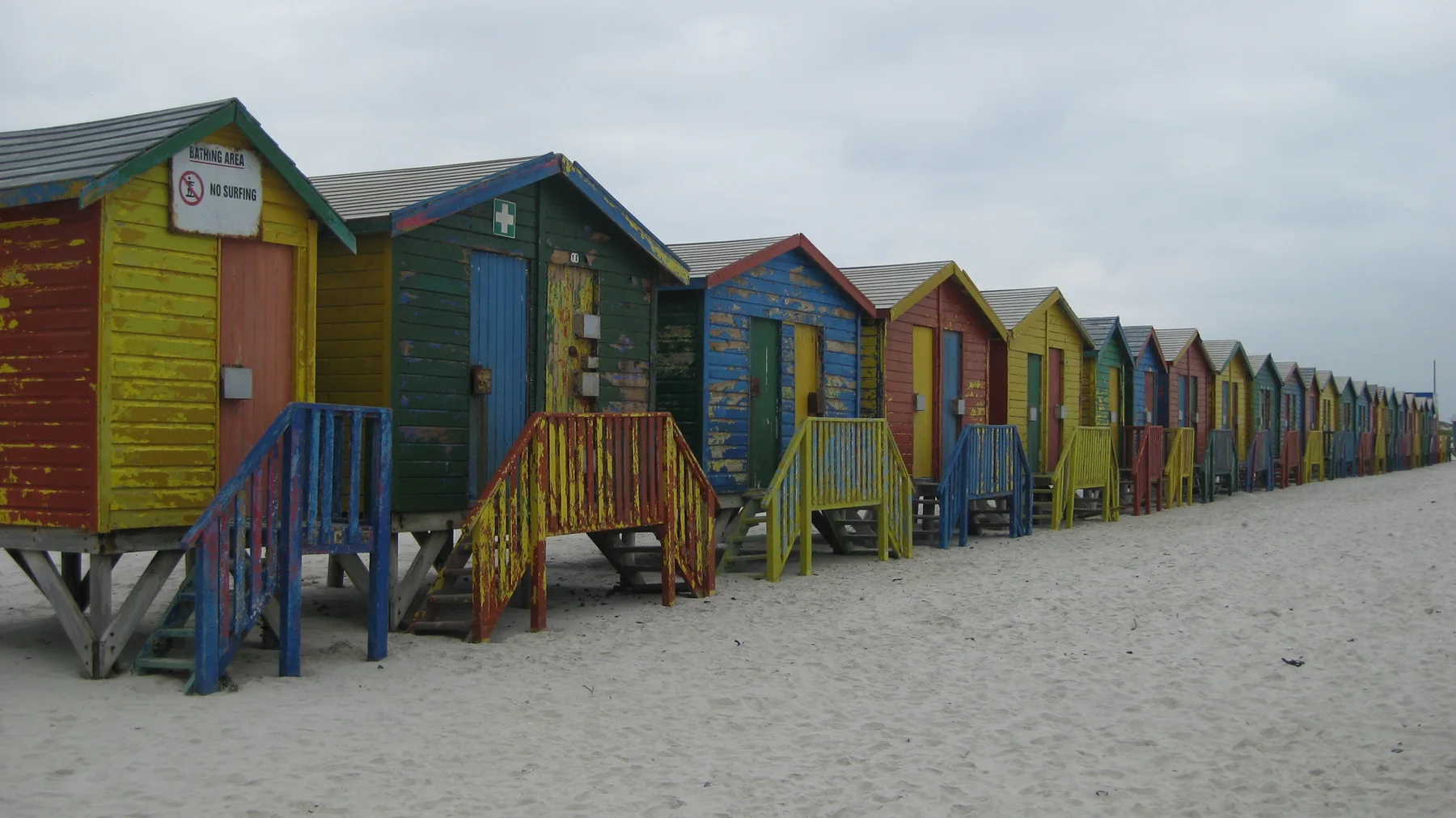 Painted wooden huts recede along the beach in alternating bright colors.