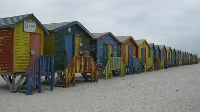 Painted wooden huts recede along the beach in alternating bright colors.