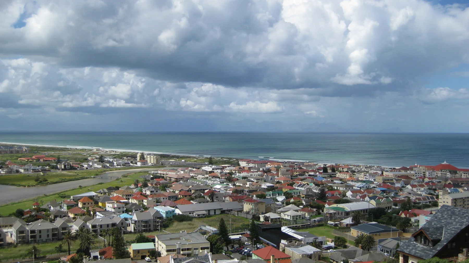 Town roofs spread toward blue water beneath towering white clouds.