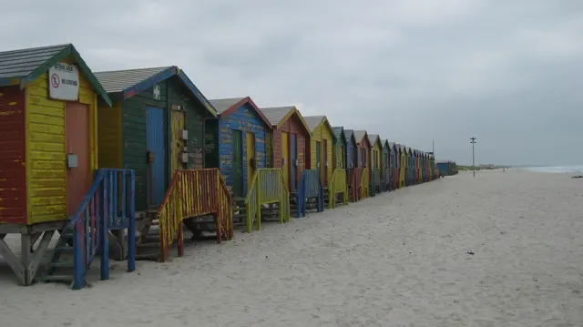 Colorful huts form a long perspective across pale sand beneath gray sky.