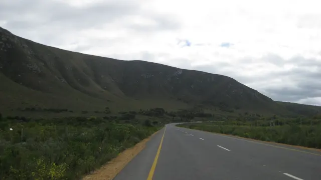 An open road follows the foot of a long mountain slope.