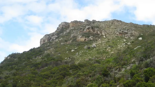 Broken rocks crown a green hillside under patches of blue sky.