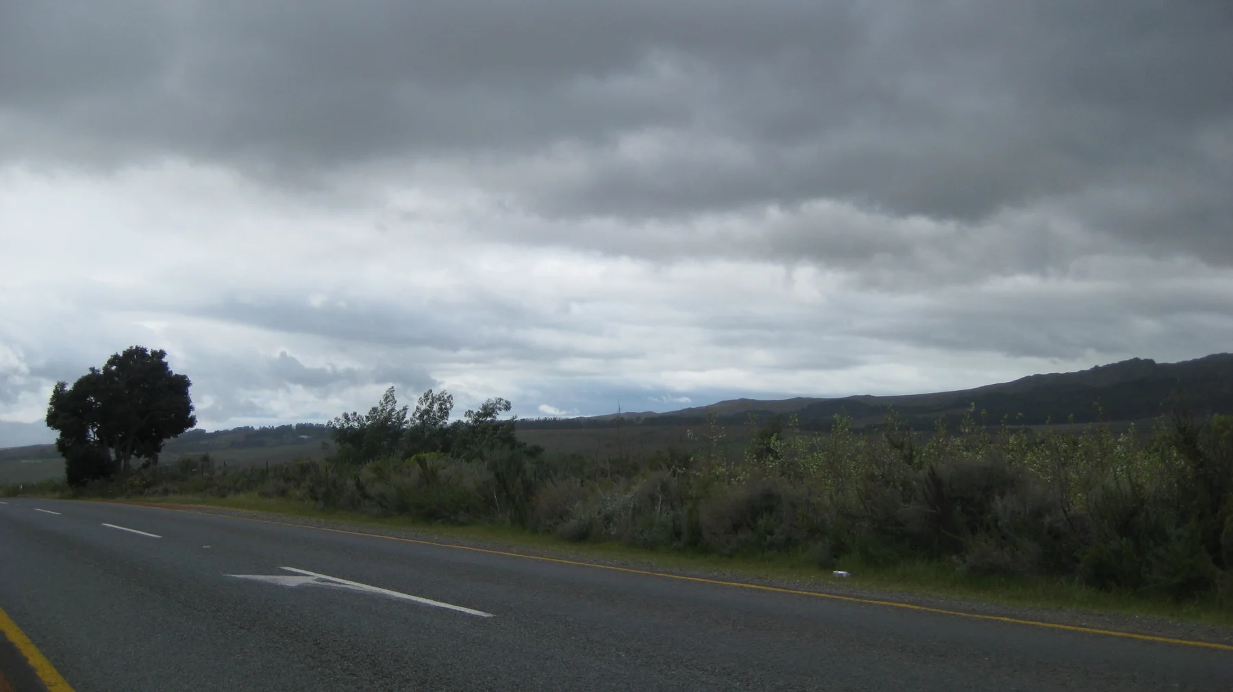 Dark clouds hang above a road bordered by low countryside.