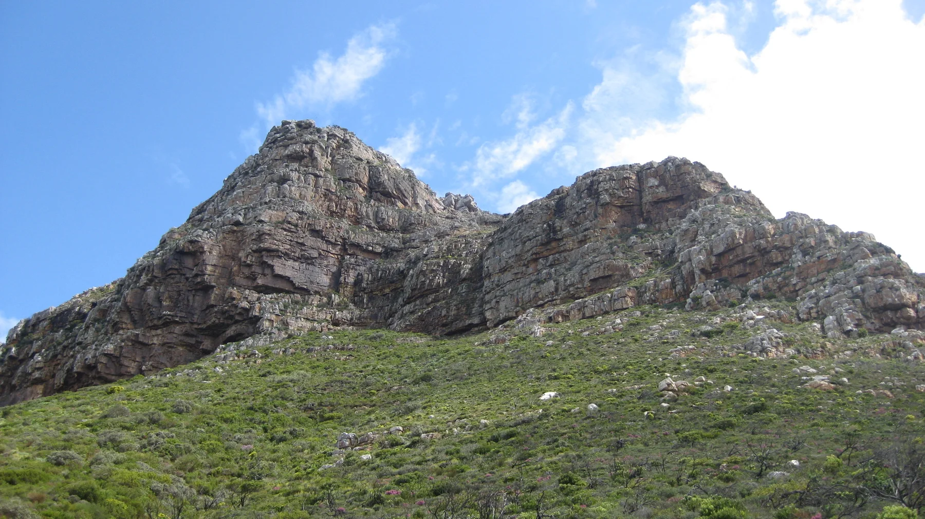 Two craggy summits rise above a green slope against blue sky.