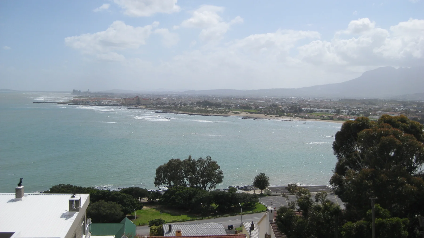A wide curving bay opens beyond foreground rooftops and trees.
