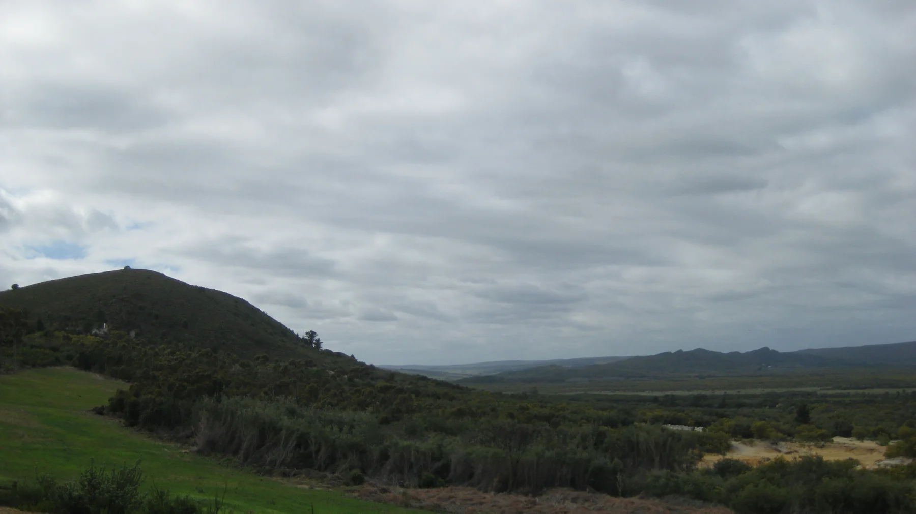Low hills and scrubland stretch beneath a thick gray cloud layer.