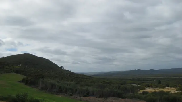 Low hills and scrubland stretch beneath a thick gray cloud layer.