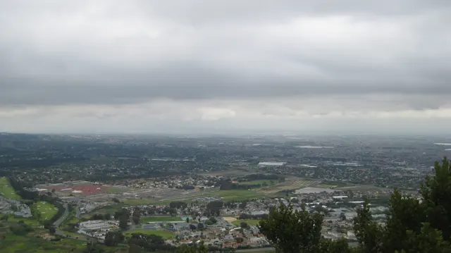 Buildings and green spaces spread across a valley beneath a low cloud ceiling.