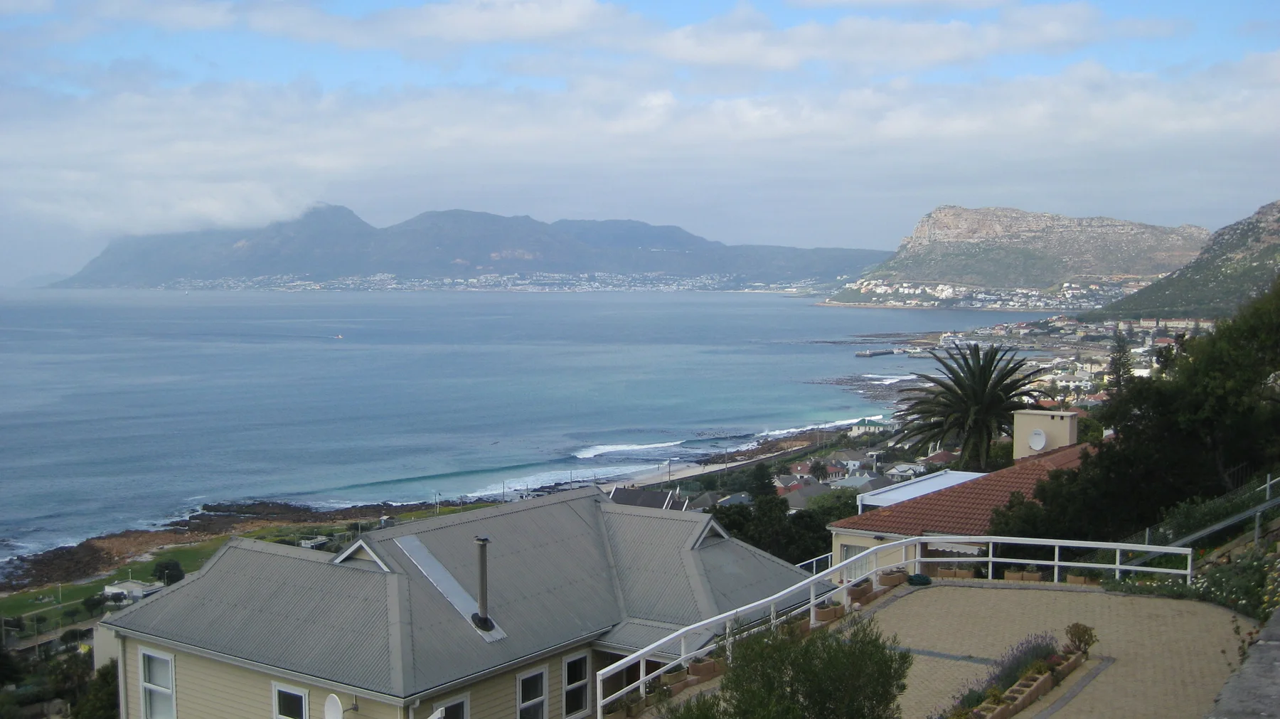 Foreground roofs overlook blue water and a distant mountain coast.