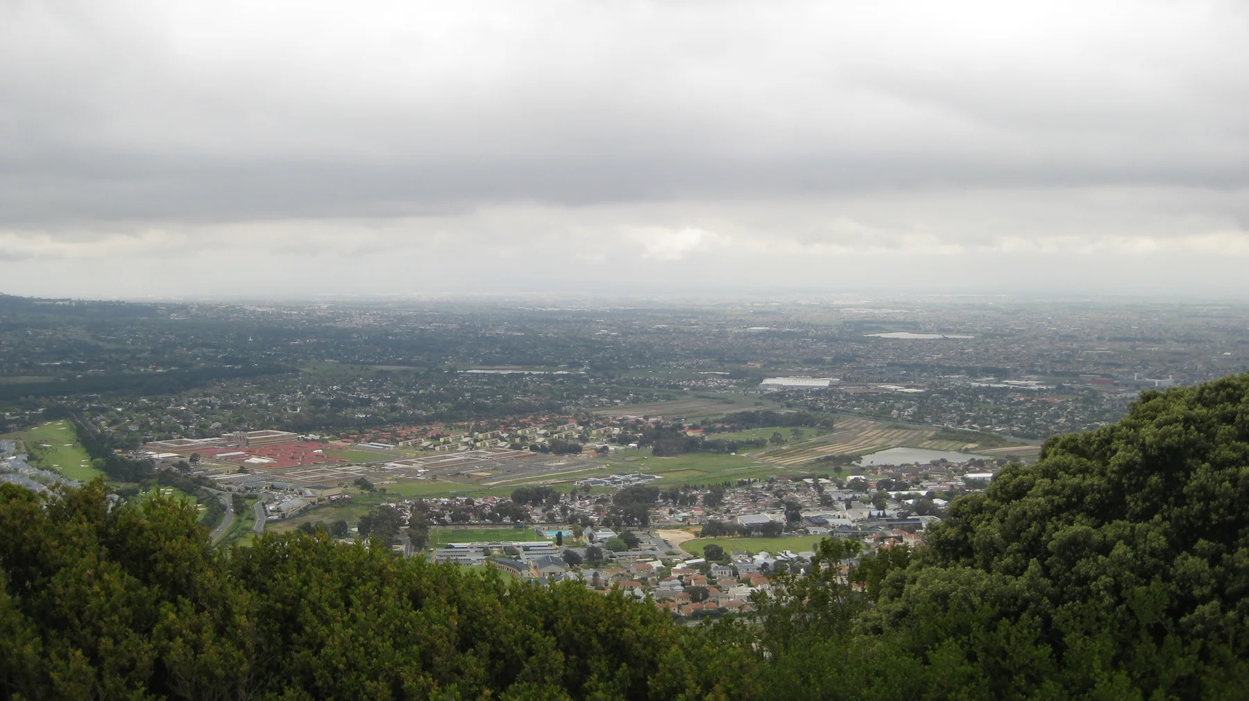 A broad developed valley lies below a pale cloudy sky.