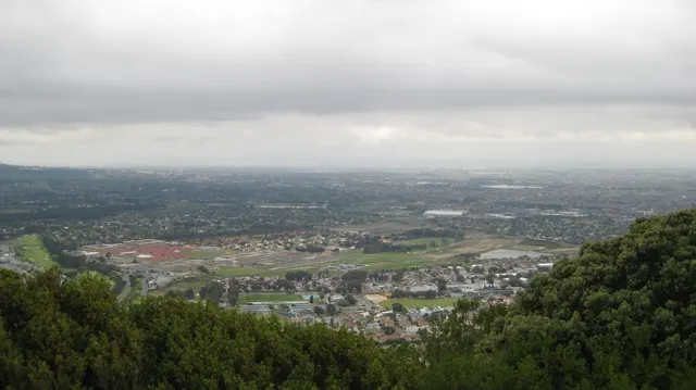 A broad developed valley lies below a pale cloudy sky.