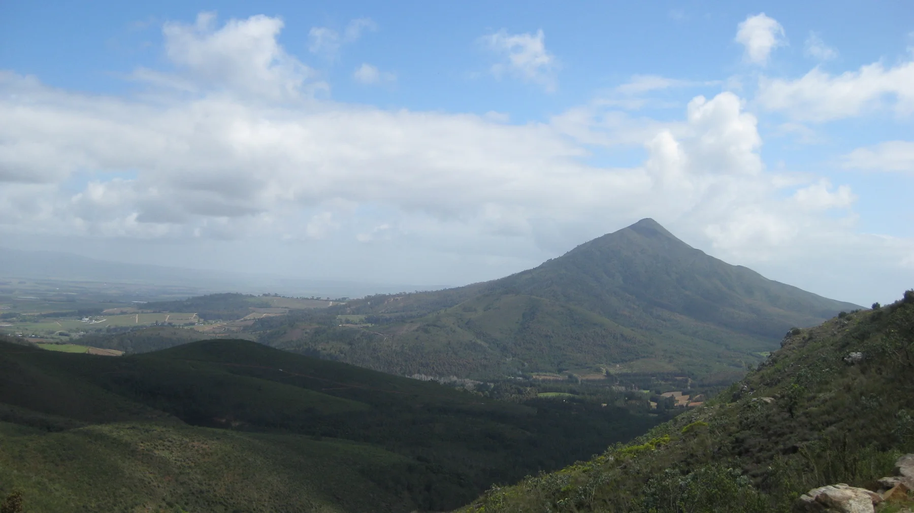 A pointed peak rises above dark rolling hills beneath scattered clouds.