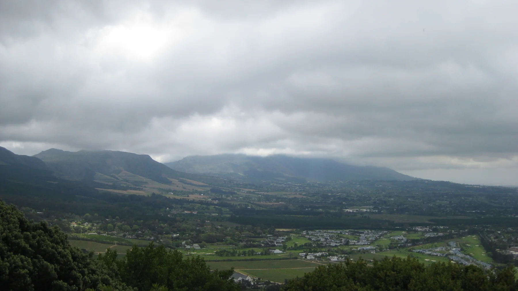 Fields spread below mountain slopes wrapped in low cloud.