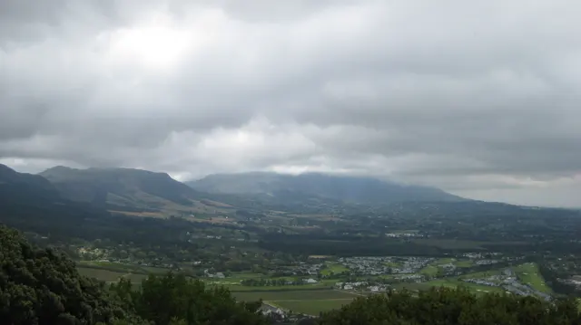 Fields spread below mountain slopes wrapped in low cloud.