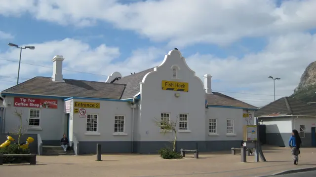 A white roadside building has a curved gable and a row of small windows.