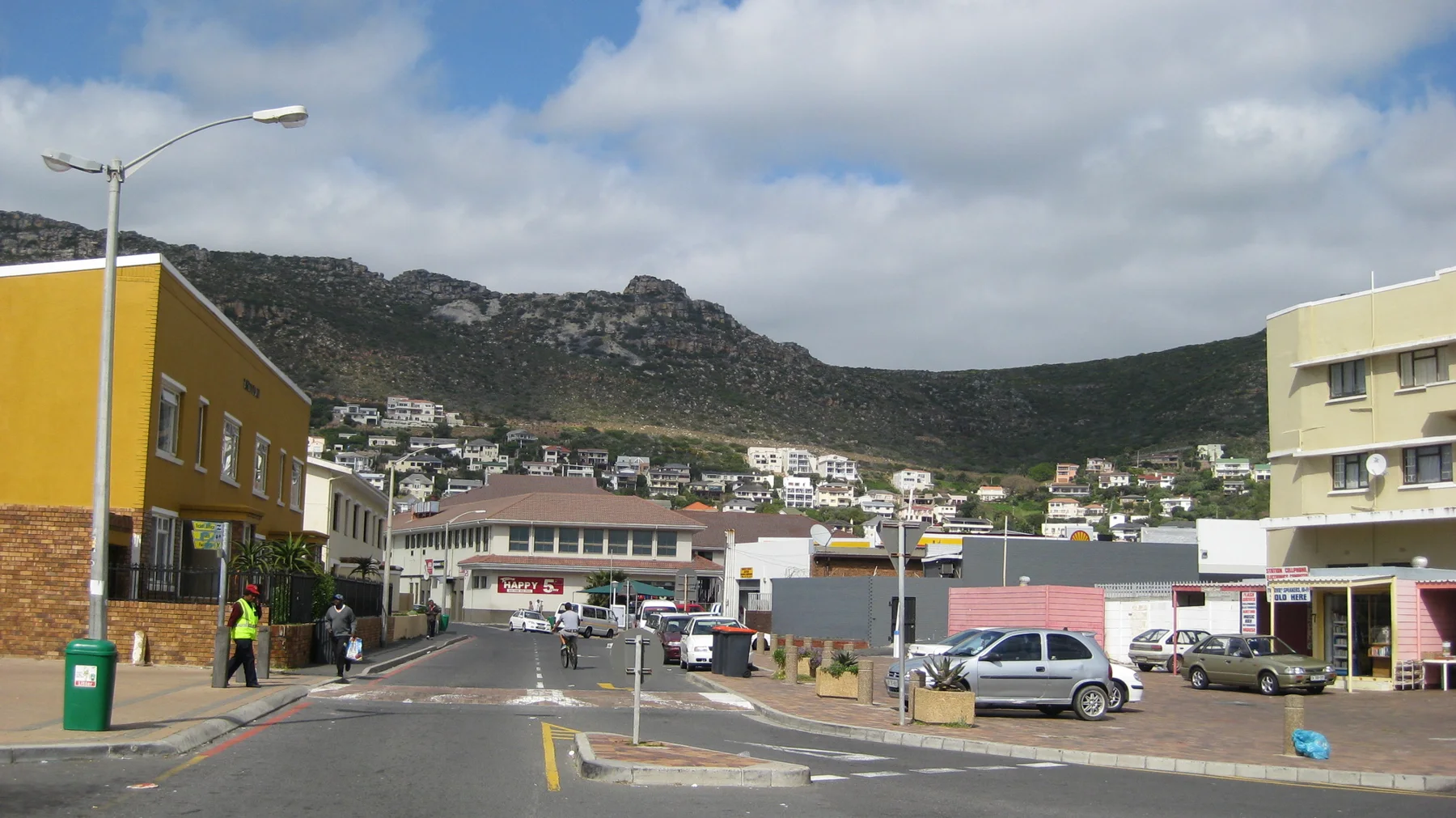 Low shops line a street below a rocky mountain ridge.
