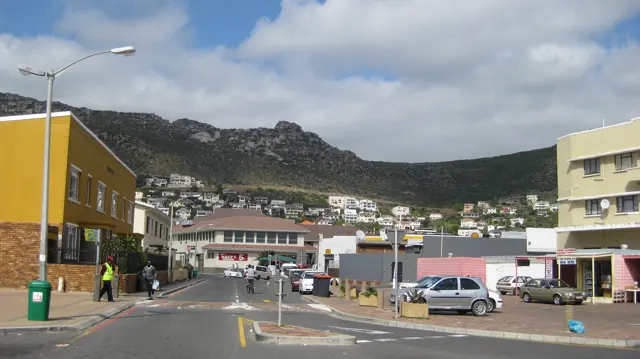Low shops line a street below a rocky mountain ridge.