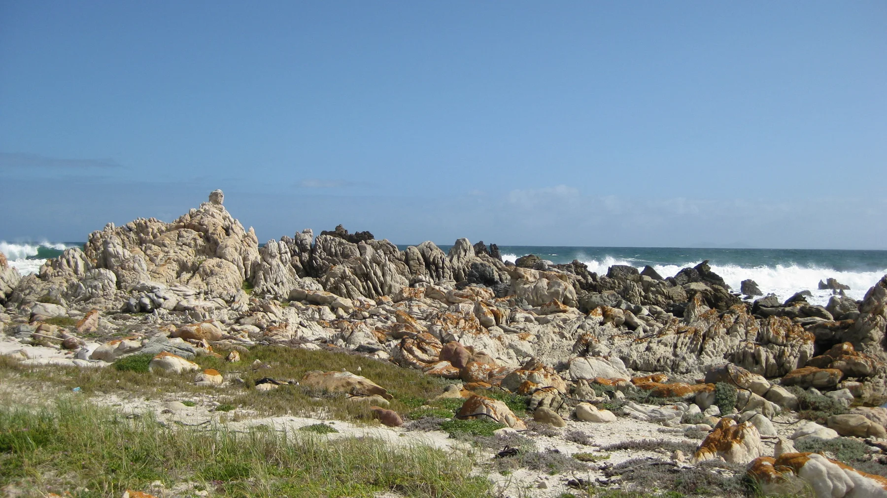 Pale jagged rocks line the coast under a clear blue sky.