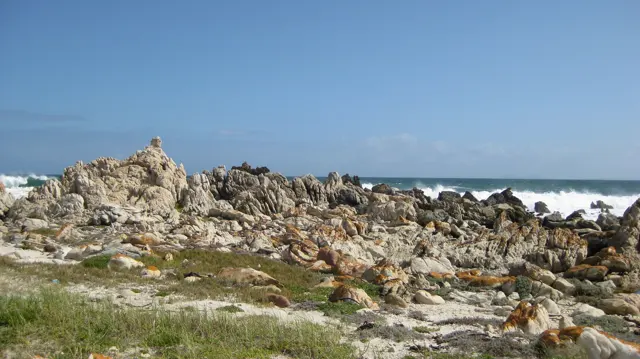 Pale jagged rocks line the coast under a clear blue sky.