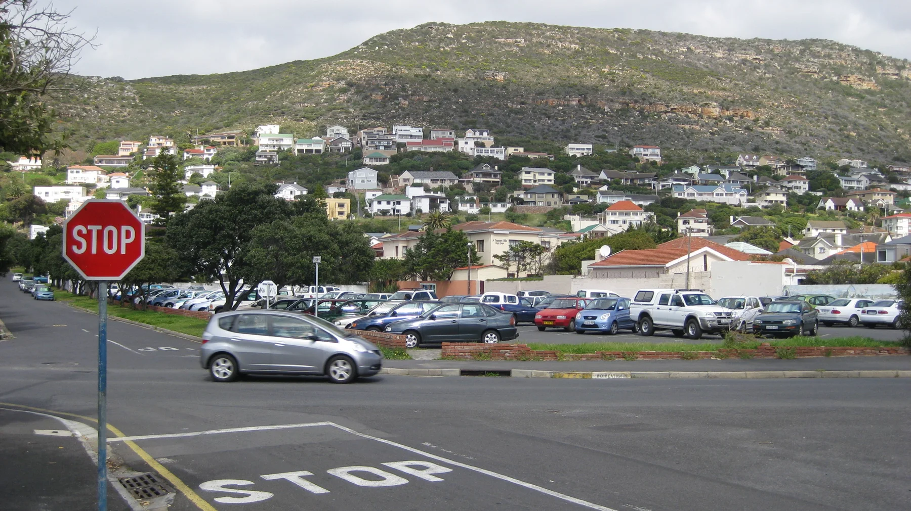 A stop sign faces traffic below houses scattered across a hillside.